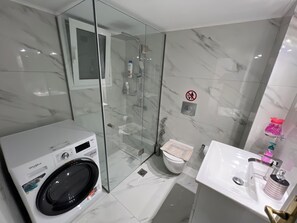 A modern bathroom with a glass-enclosed shower, a Whirlpool steam washer, a toilet with a patterned seat cover, and a white sink with a soap dispenser. - Four Seasons Apartment in Athens (Karpenisi)