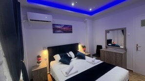 A modern bedroom with a bed, bedside tables, a dresser, a mirror, and an air conditioning unit. - Four Seasons Apartment in Athens (Karpenisi)