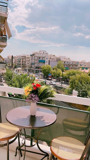 A balcony with a round table and two wicker chairs, overlooking a cityscape with buildings and a clear sky. - Four Seasons Apartment in Athens (Karpenisi)