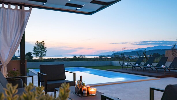 Ein Poolbereich mit Bergblick, Sitzgelegenheiten im Freien und einem Tisch mit Kerzen und Gläsern.