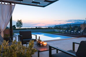 Un espace aménagé au bord de la piscine, offrant une vue sur les montagnes, avec des sièges d’extérieur et une table décorée de bougies et de verres.