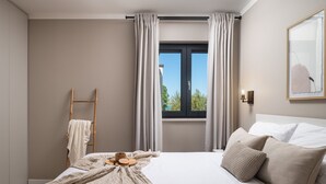 Ein Schlafzimmer mit Bett, einem Fenster mit Vorhängen, einer Holzleiter und einer Wandleuchte.