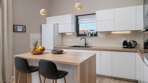 Eine moderne Küche mit einer Holzinsel, zwei schwarzen Barhocker, einer Obstschale und einer Kaffeemaschine.