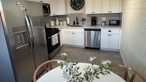 A modern kitchen with white cabinets, stainless steel appliances, a clock, and a vase with flowers on the table. - Charming 3-bedroom house with AC and WiFi in delightful Phoenix (Phoenix)
