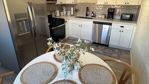 A modern kitchen with white cabinets, stainless steel appliances, a round dining table with woven placemats, and a wall clock. - Charming 3-bedroom house with AC and WiFi in delightful Phoenix (Phoenix)