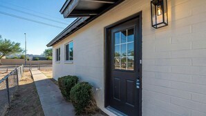 A single-story building with a black front door, a small window, and a wall-mounted light fixture. - Charming 3-bedroom house with AC and WiFi in delightful Phoenix (Phoenix)