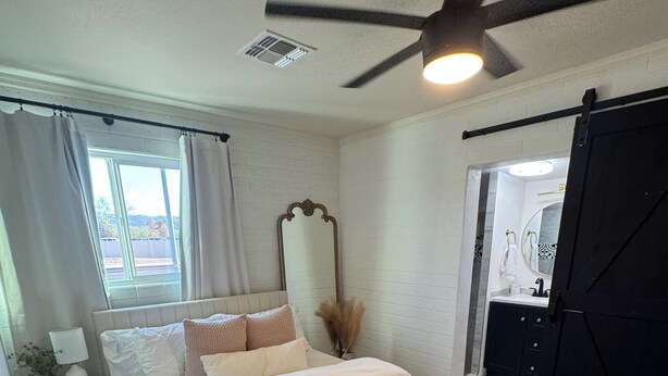 A bedroom with a bed, a ceiling fan, a window with curtains, a bedside table with a lamp, and a mirror. - Charming 3-bedroom house with AC and WiFi in delightful Phoenix (Phoenix)