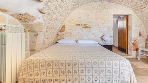 A bedroom with a stone ceiling, a bed with a patterned bedspread, a wooden door, and a radiator. - 3740 AM Carrone - Appartamento 2 (Carovigno)
