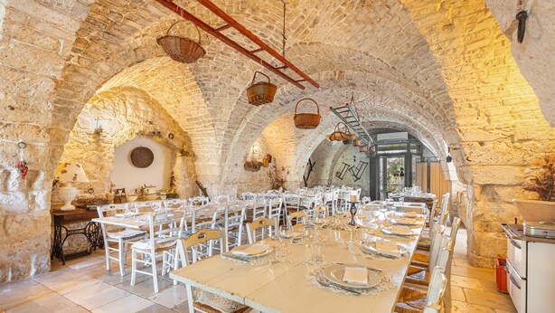 A long dining table set for a meal in a stone-walled room with arched ceilings and hanging baskets. - 3740 AM Carrone - Appartamento 2 (Carovigno)