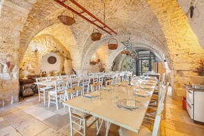 A long dining table set for a meal in a stone-walled room with arched ceilings and hanging baskets. - 3740 AM Carrone - Appartamento 2 (Carovigno)