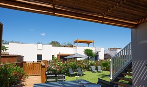 A covered outdoor patio with a wooden deck, a barbecue area, and two lounge chairs.