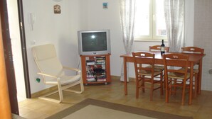 Un soggiorno con televisione, una libreria, un tavolo da pranzo con sedie e una finestra con tende.