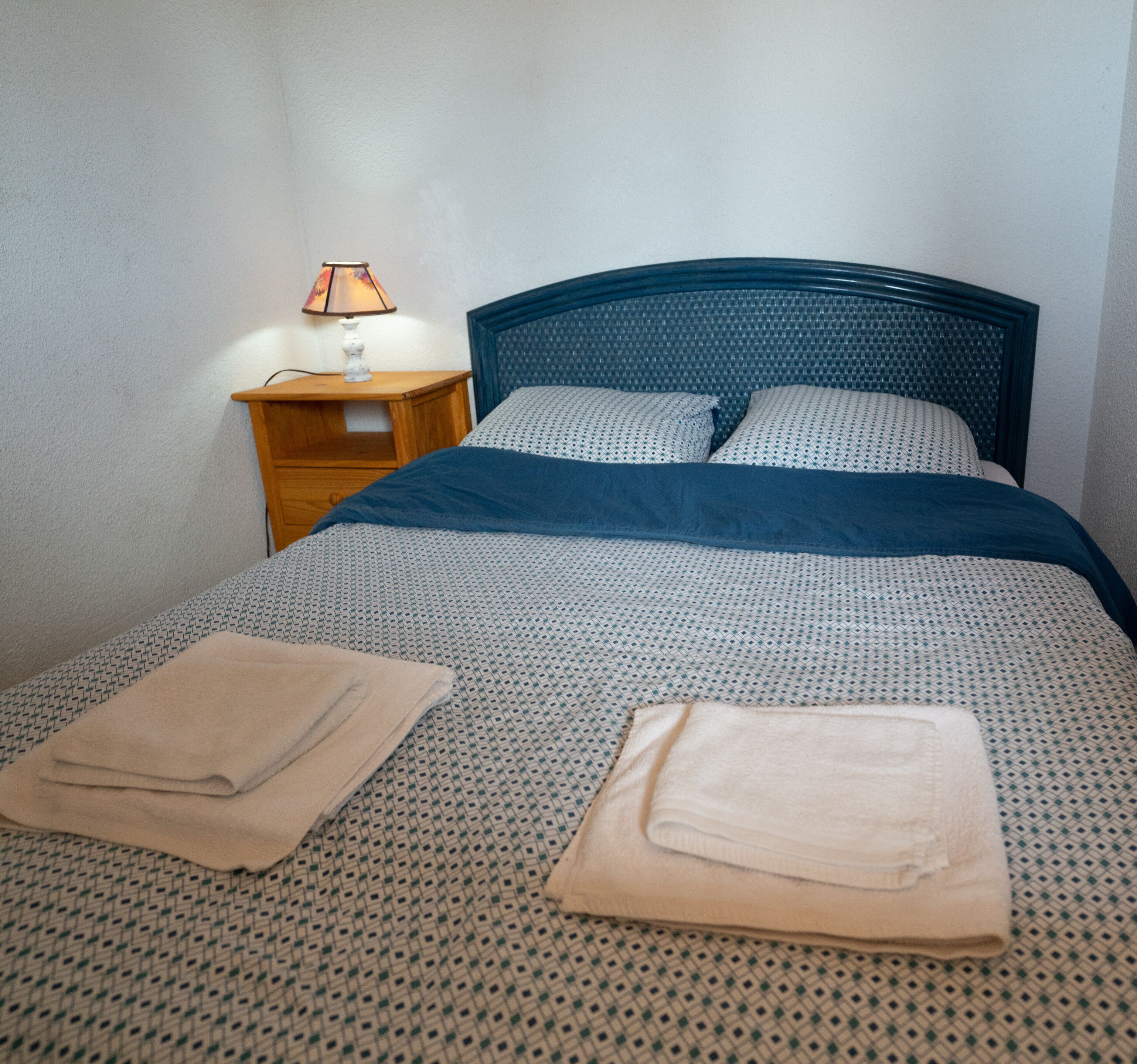 Una cama bien hecha con una colcha estampada y dos toallas dobladas.