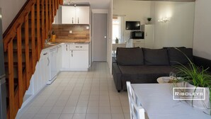 Eine moderne Küche mit weißen Schränken, einer Holztreppe und einem Wohnbereich mit Sofa und Esstisch.