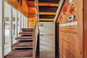 Una cocina compacta con refrigerador, paredes de madera y una escalera que sube a un nivel superior.