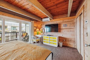 Un dormitorio con cama, televisión, cómoda y ventana con vistas a un balcón.