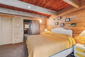 A wooden cabin bedroom with a bed, bedside lamps, a wooden wardrobe, and framed fish pictures on the wall.