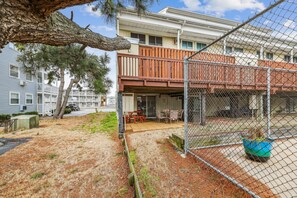 Un espacio exterior cercado con una terraza de madera, una mesa y sillas, y una planta en maceta.