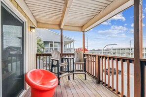Una terraza de madera con dos sillas Adirondack y un taburete rojo.