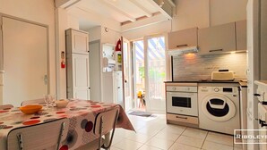 Una cucina con lavatrice, zona pranzo con tavolo e sedie, e una porta che dà su un balcone.