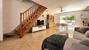 A spacious living room with a wooden staircase, a dining area, and a large window providing natural light. - Riboleys - Villa avec clim et piscine privée (Vias)
