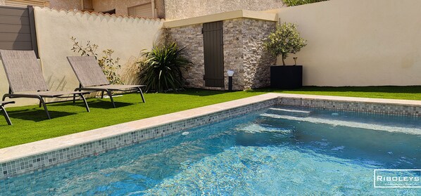 A swimming pool with a tiled edge, surrounded by a well-maintained lawn and a stone wall.