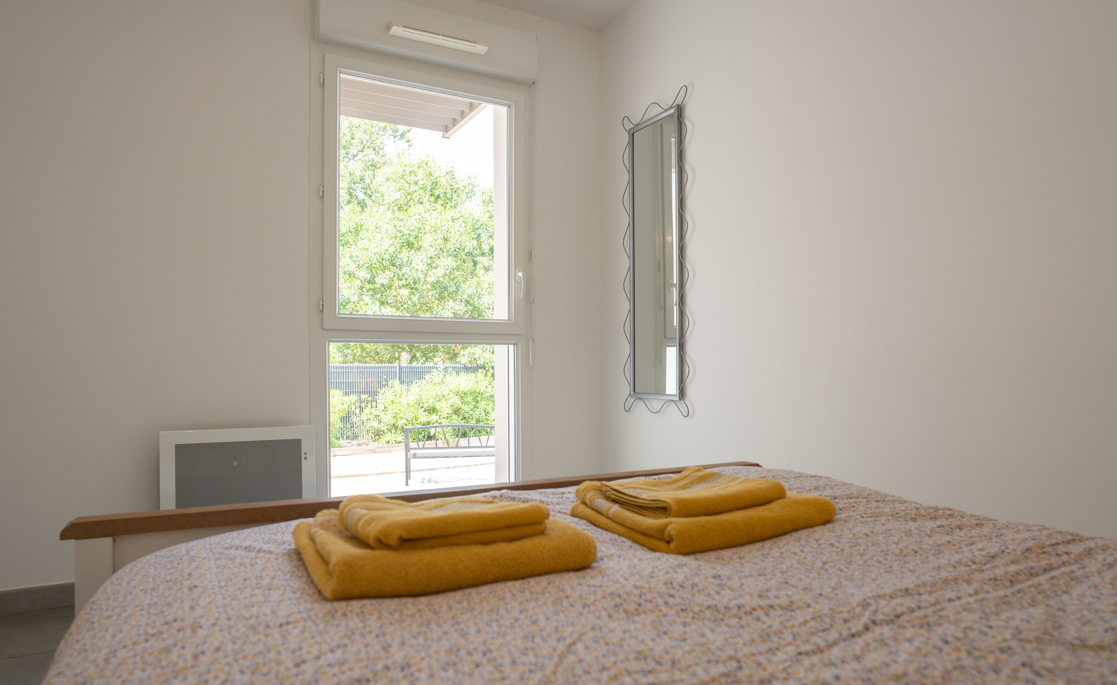 A bedroom with a bed, two windows, a radiator, and a mirror.
