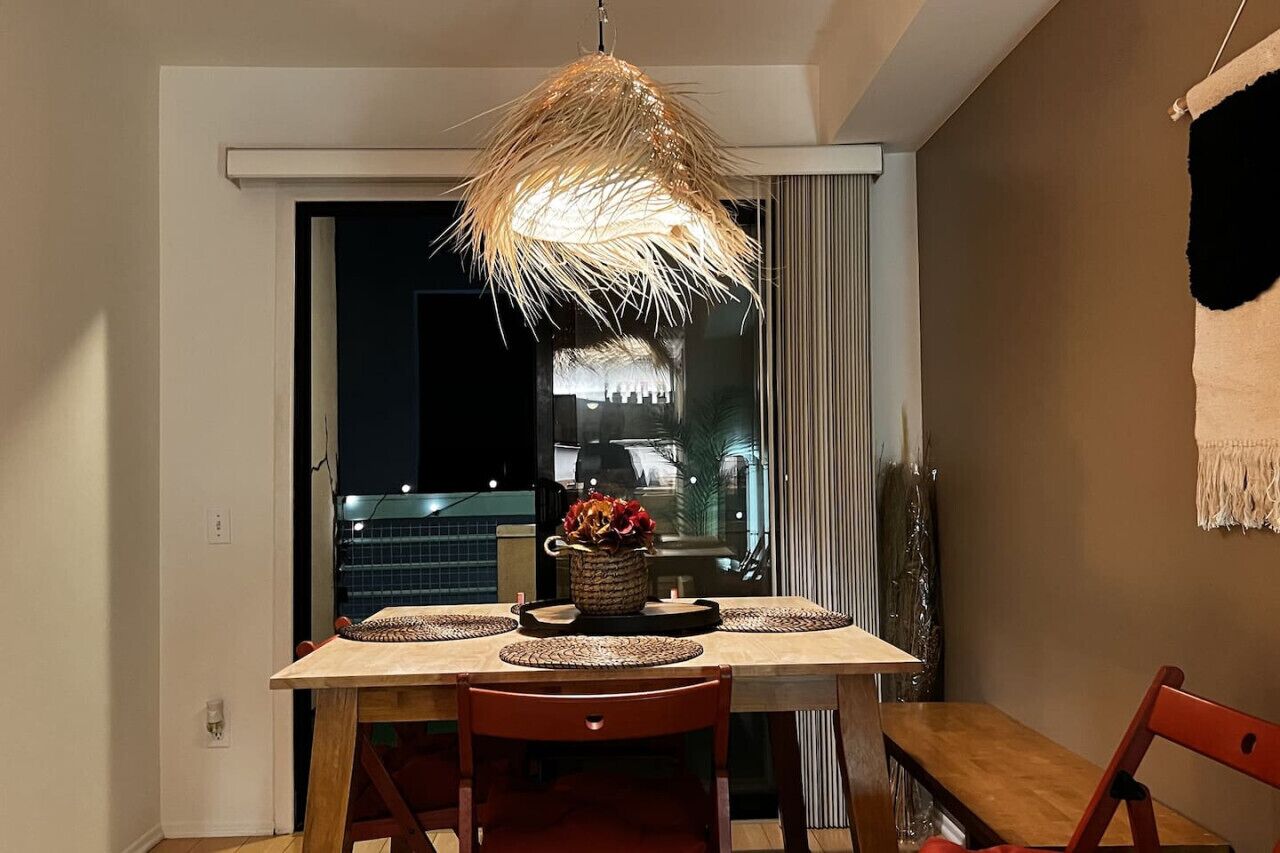 Un comedor con una mesa de madera, individuales tejidos y una lámpara colgante.