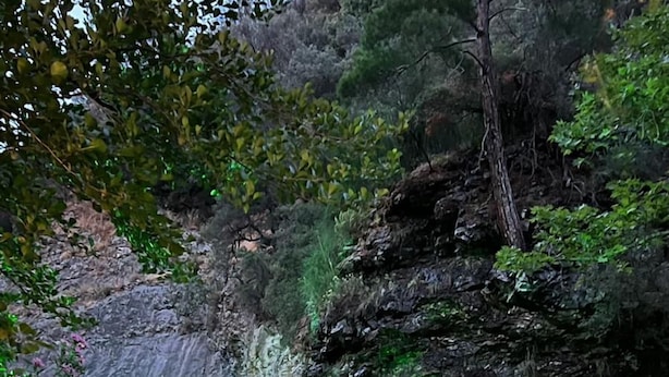 Una mesa y dos sillas sobre un saliente rocoso con vistas a un río y una cueva al fondo.