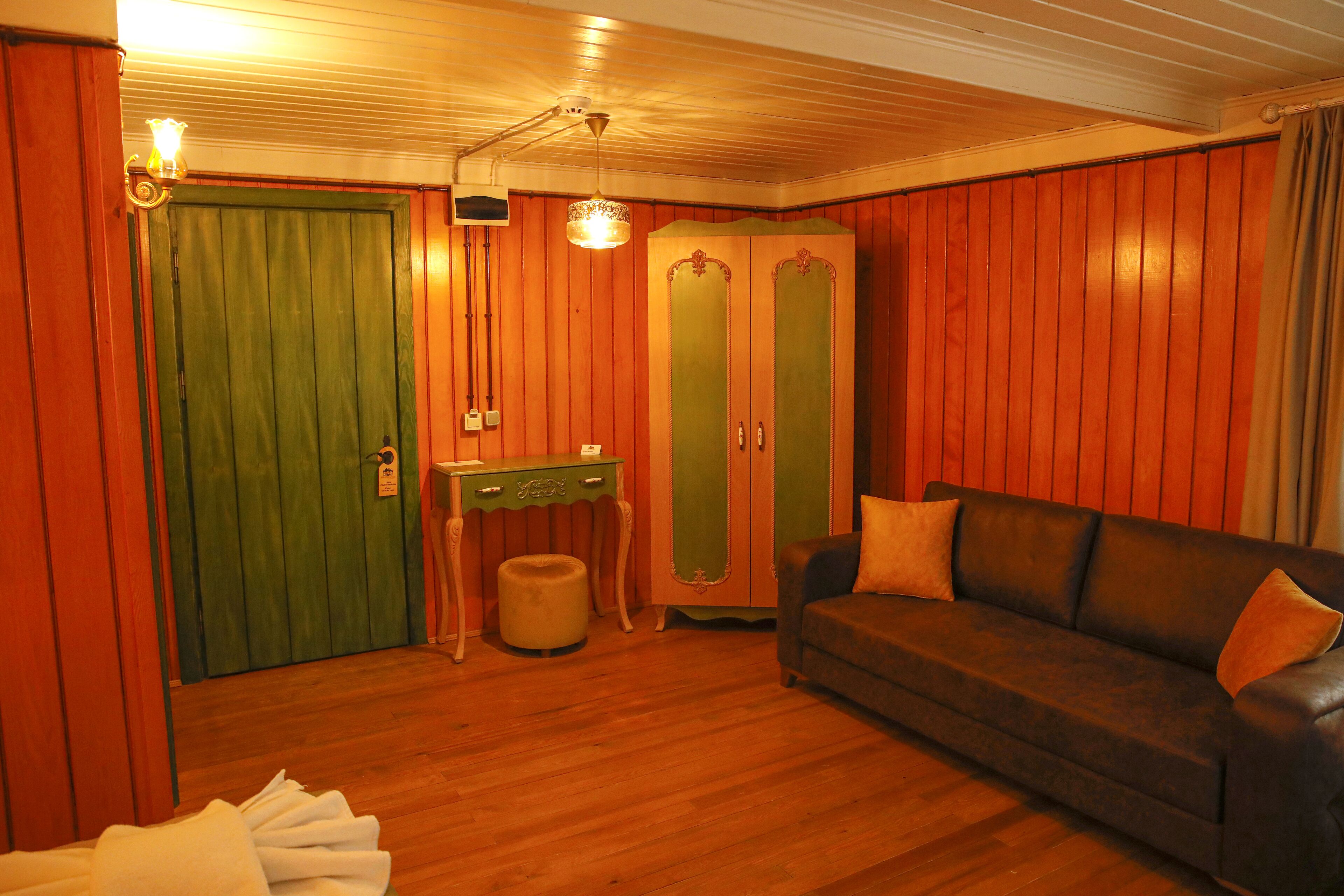A room with wooden walls, a green door, a brown leather sofa, and a small table with a lamp.
