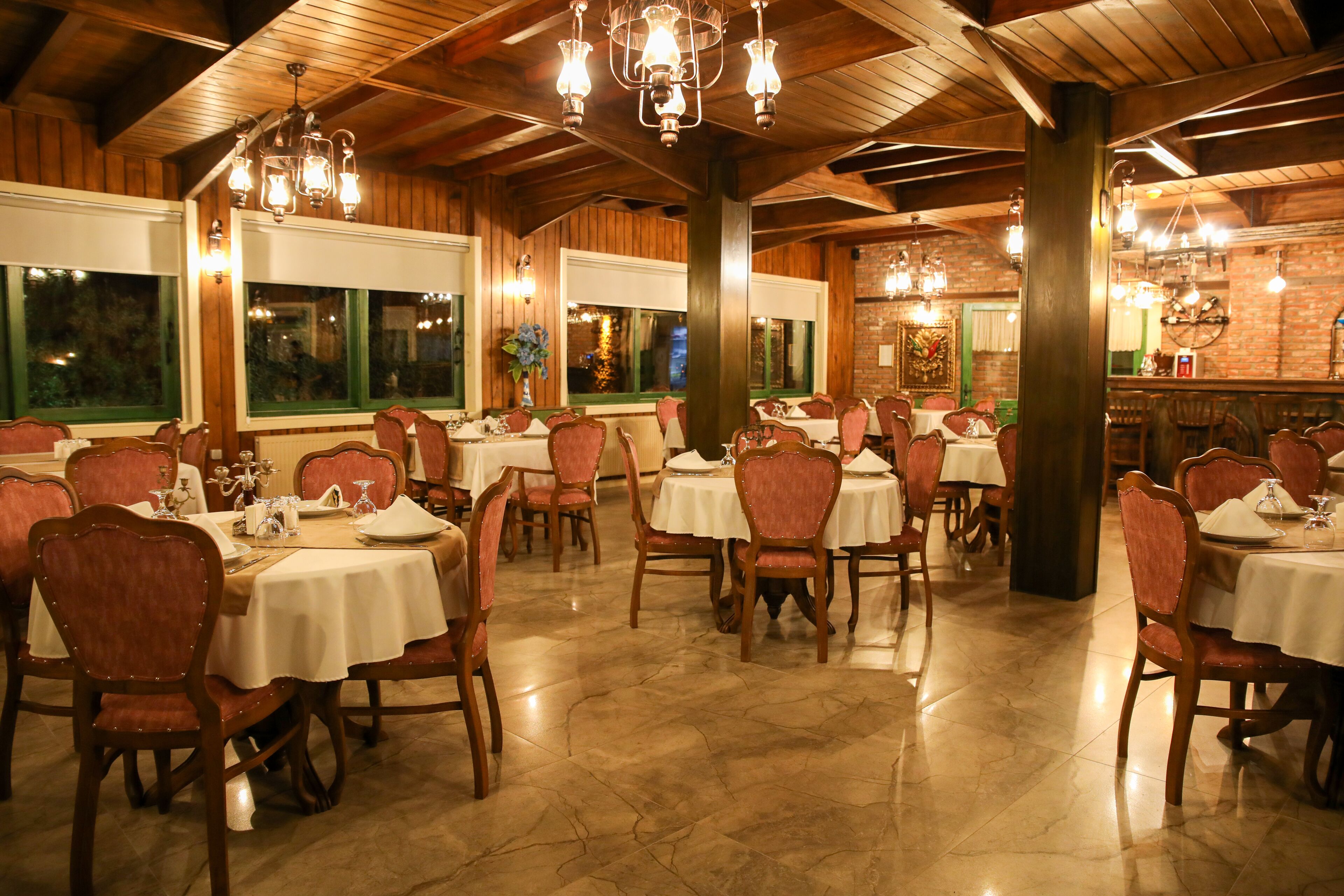 Un restaurante con varias mesas y sillas, vigas de techo de madera y amplios ventanales.