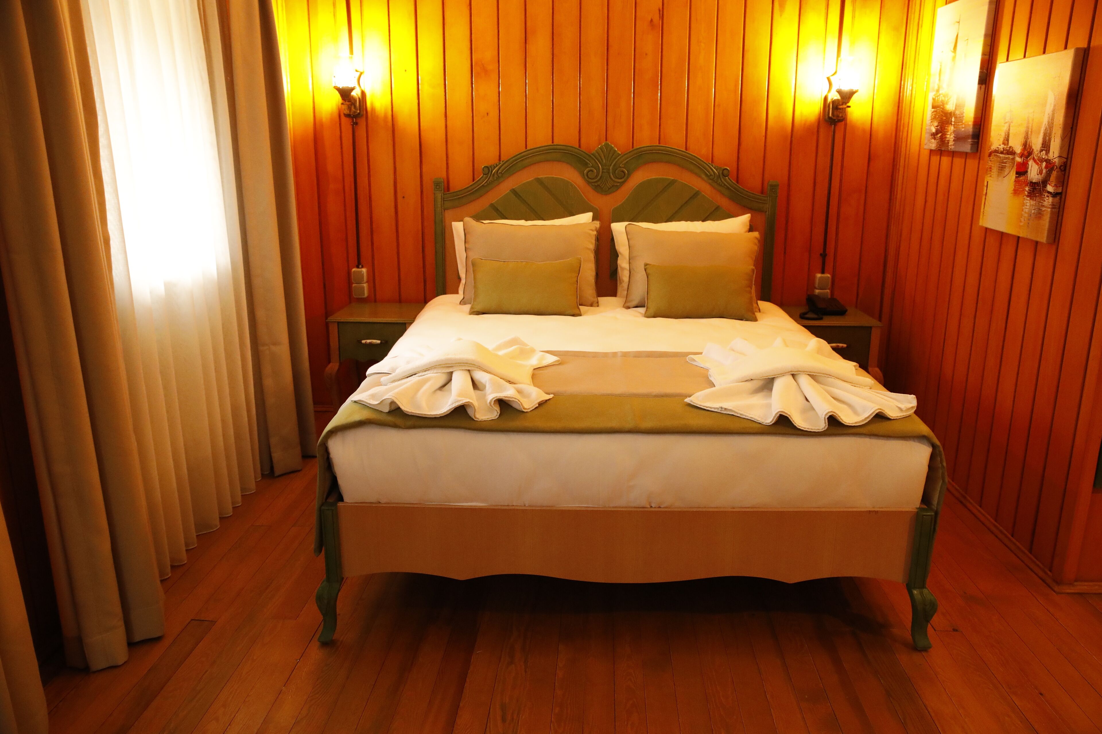 A neatly made bed with a green headboard, two bedside tables with lamps, and a wooden floor.