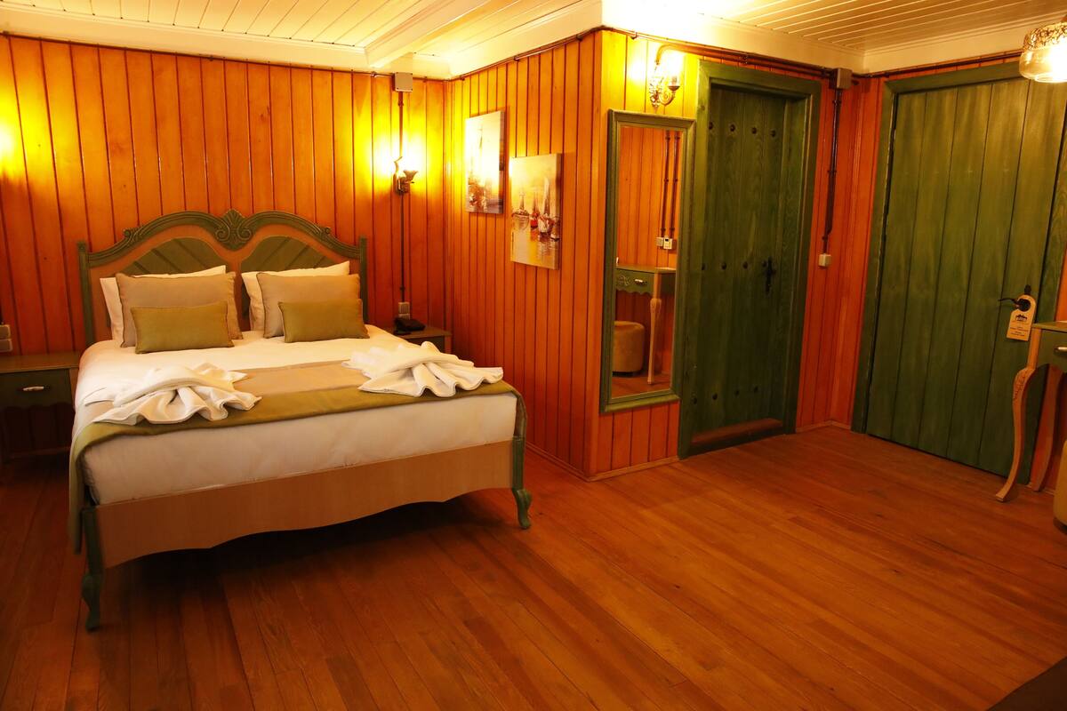 A wooden-paneled bedroom with a bed, two wall sconces, and a green door.