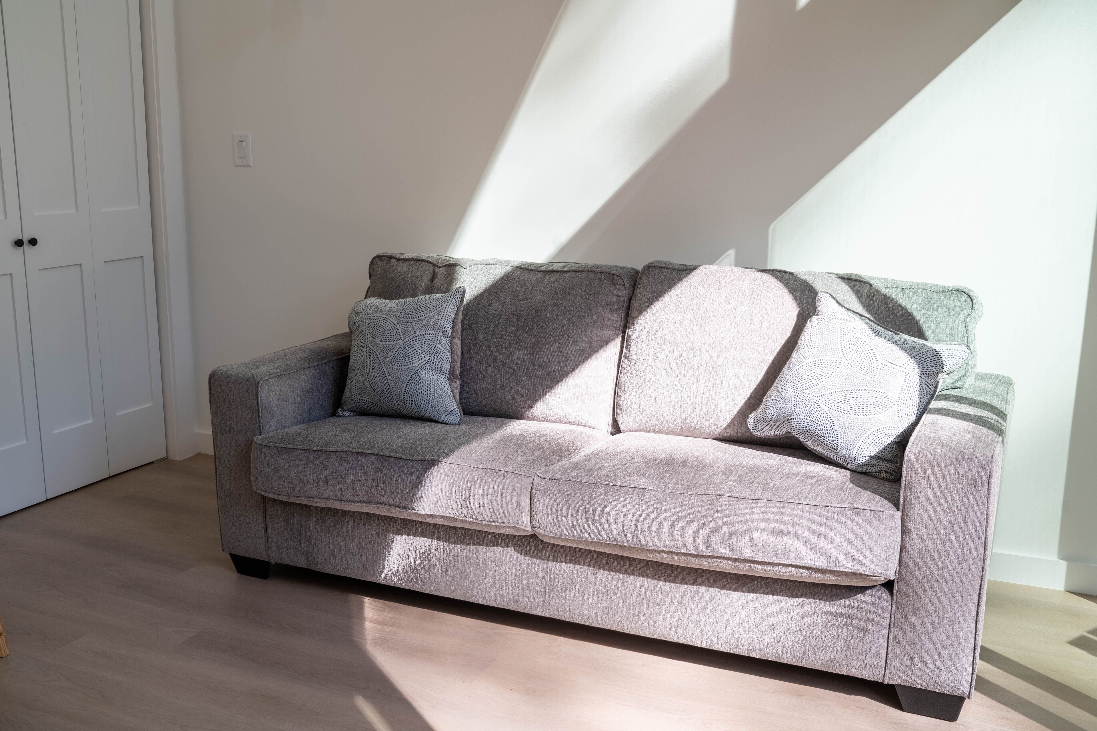 A grey sofa with patterned cushions in a room with wooden flooring and white walls.