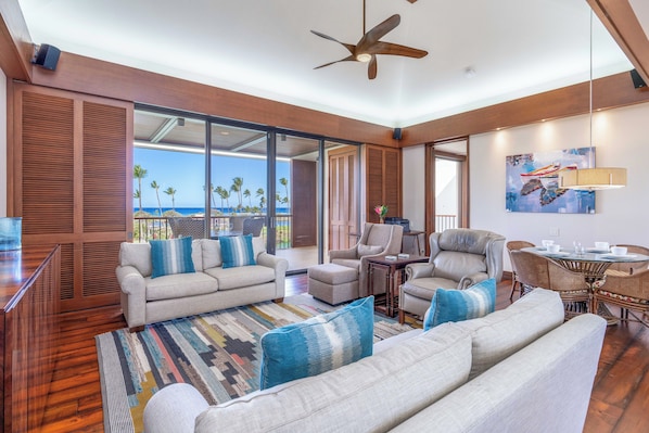 A spacious living area with a large sofa set, a dining table with chairs, and a ceiling fan.