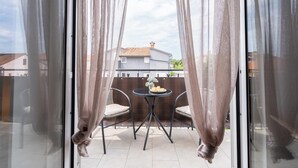 Un balcón con una mesa, sillas, cortinas y vista a una casa al fondo.
