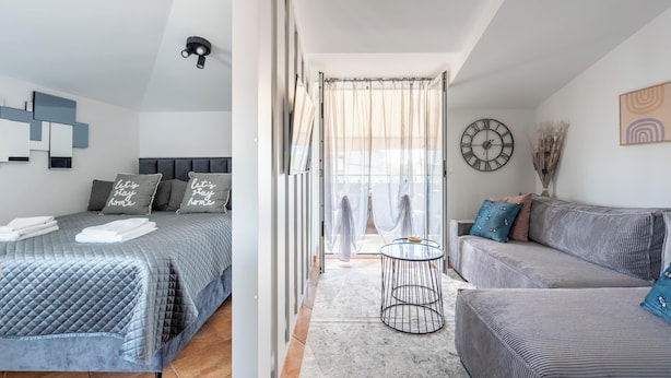 Un dormitorio moderno con cama, sofá, una mesita y una ventana con cortinas.