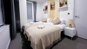 Una habitación de hotel moderna con dos camas, un cabecero de madera, una mesita de noche pequeña con una lámpara y una ventana con cortinas.