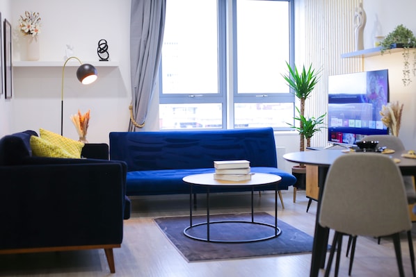 A modern living room with a blue sofa, a round coffee table, and a TV on a stand. - Cozy Luxury City Apartment in Central Bracknell (Bracknell)