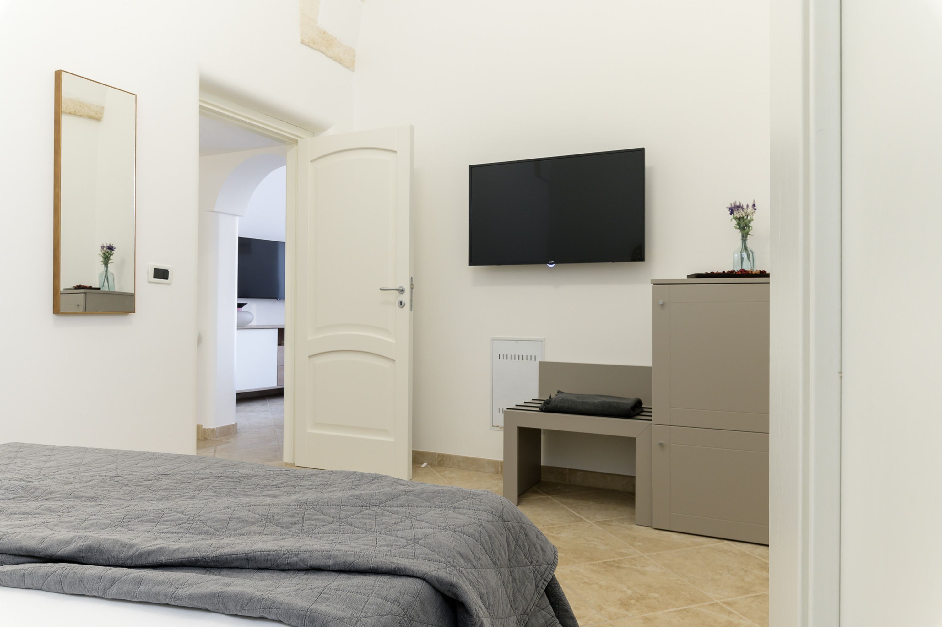 Une chambre à coucher comprenant un lit, un téléviseur fixé au mur, une armoire et une porte donnant sur une autre pièce.