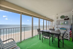 A balcony with a view of the beach, a table with chairs, and a shelf with decorative items. - English Towers-Dreamy Ocean Views in this 3 Bedroom Condo with Indoor Pool! (Ocean City)