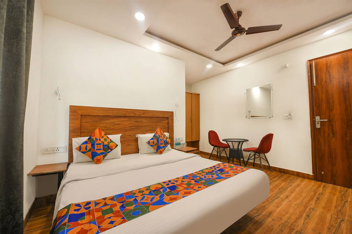 A hotel room with a bed, a ceiling fan, a small table with chairs, and a wooden door.