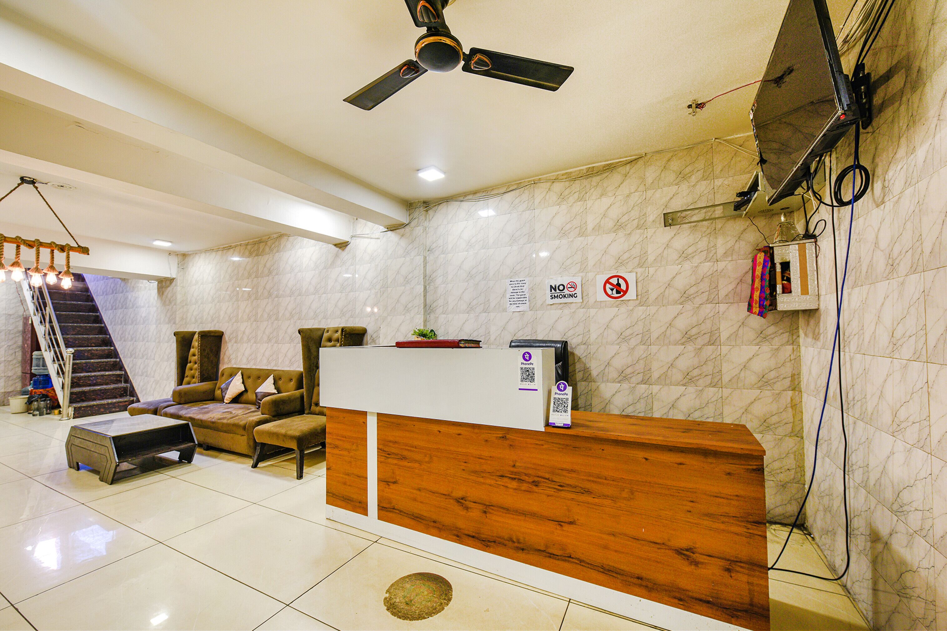 A hotel reception area with a wooden reception desk, a sofa, a coffee table, and a ceiling fan.