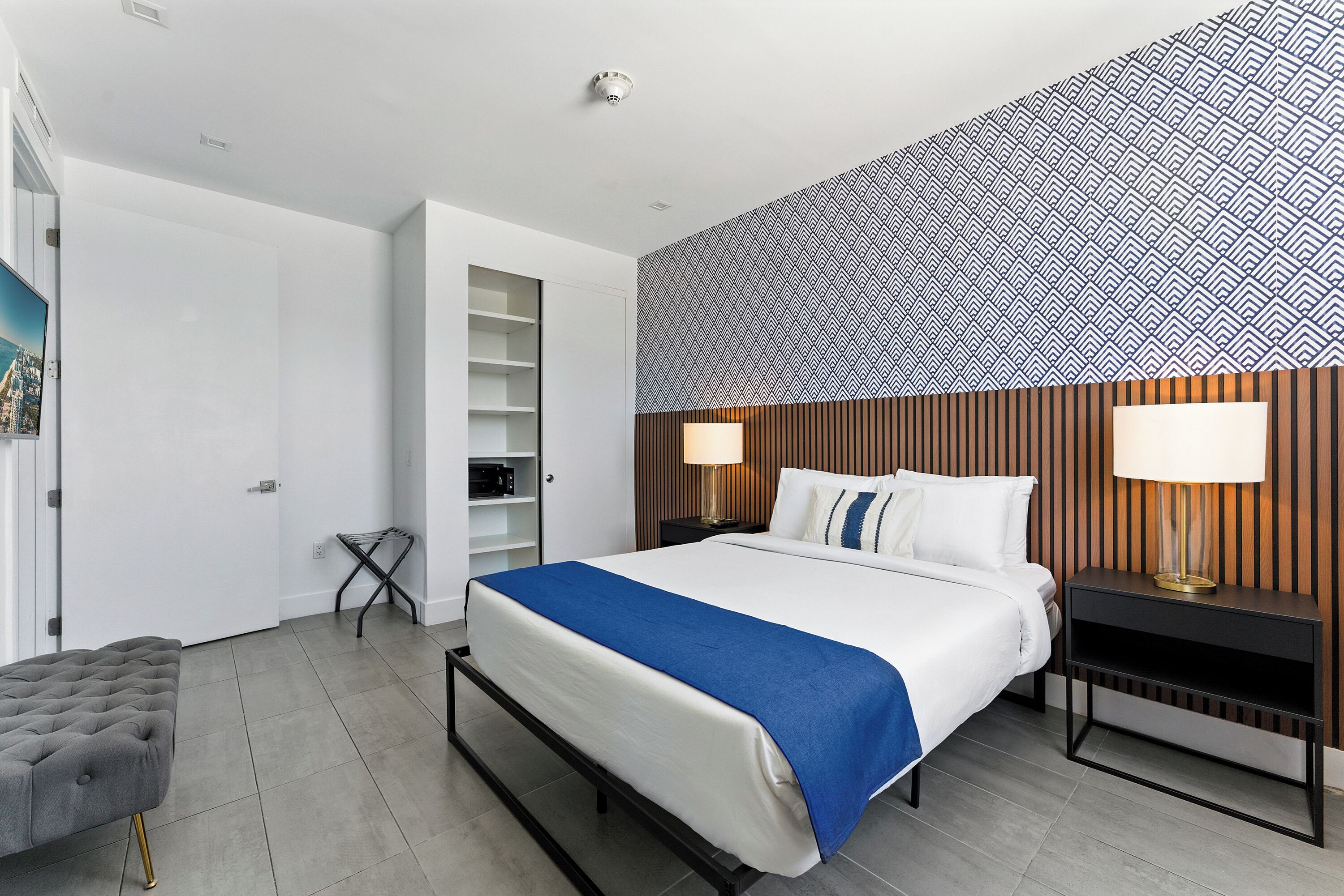 A modern hotel room with a large bed, bedside lamps, a wooden headboard, and a view of the city through the window.