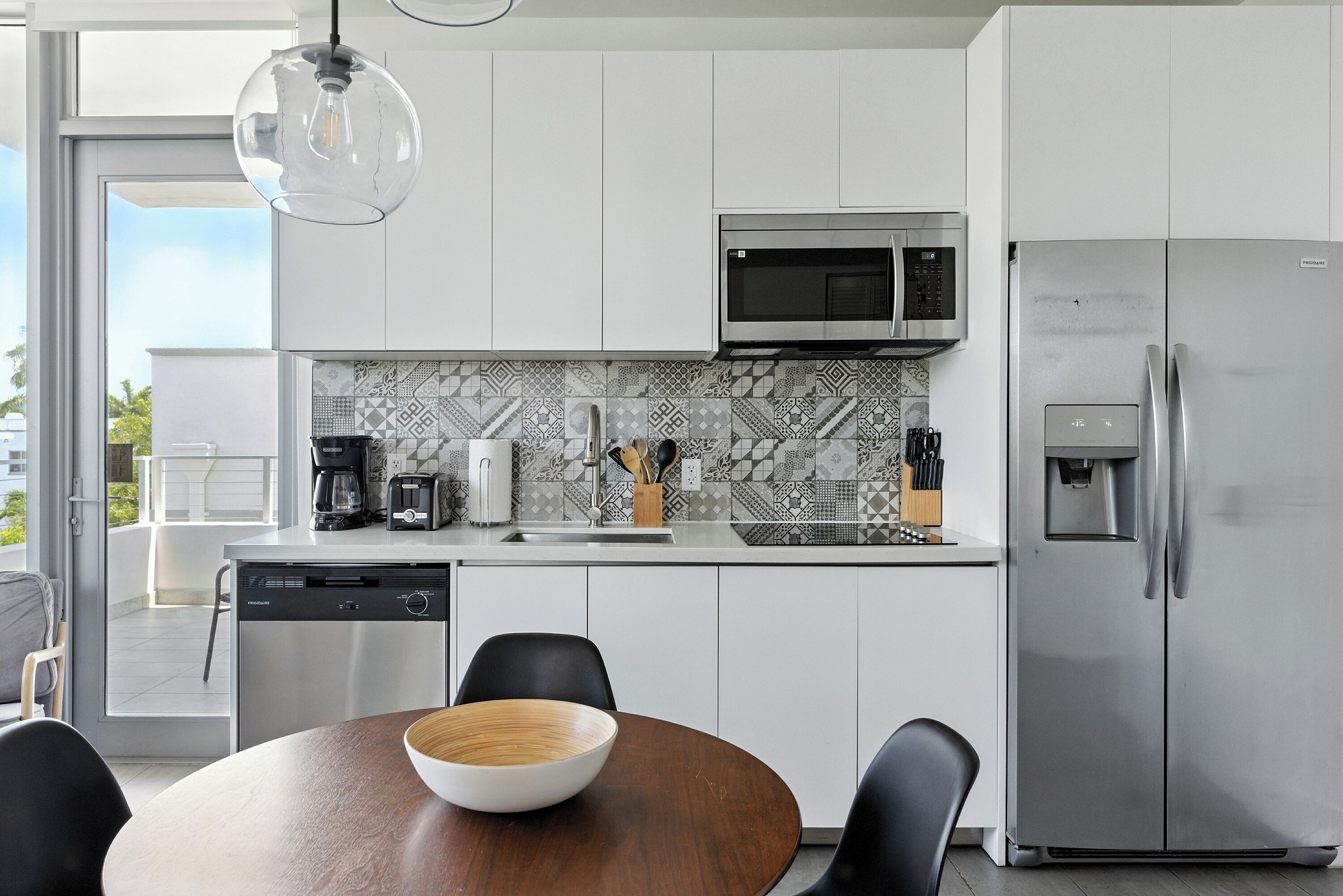 A modern kitchen with white cabinets, a stainless steel refrigerator, a microwave, and a coffee maker.