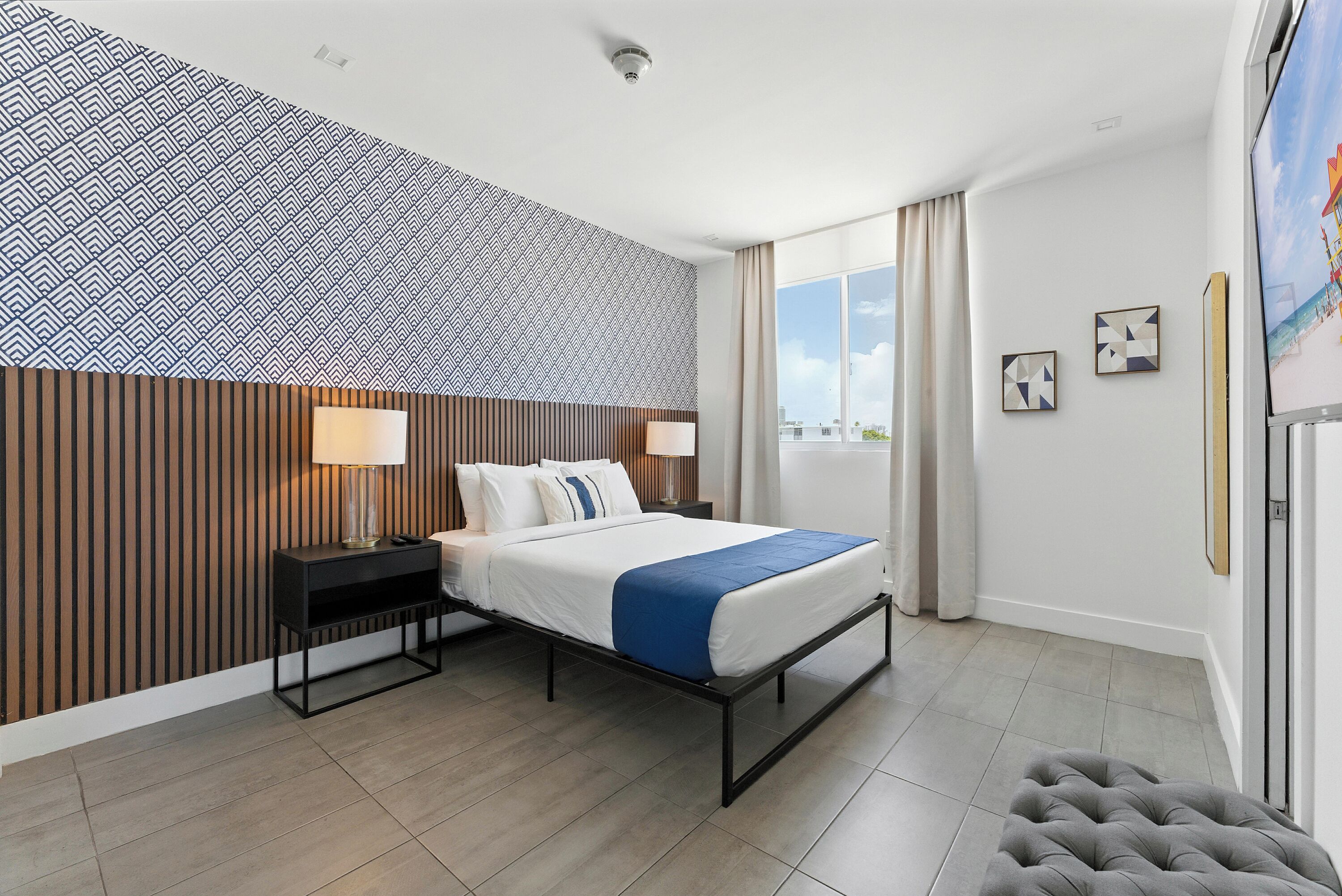 Ett modernt hotellrum med en säng, sänglampor, en tv och utsikt över staden.