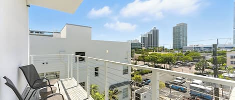 Un balcón con dos sillas y vistas a un paisaje urbano con edificios altos y una calle con vehículos estacionados.