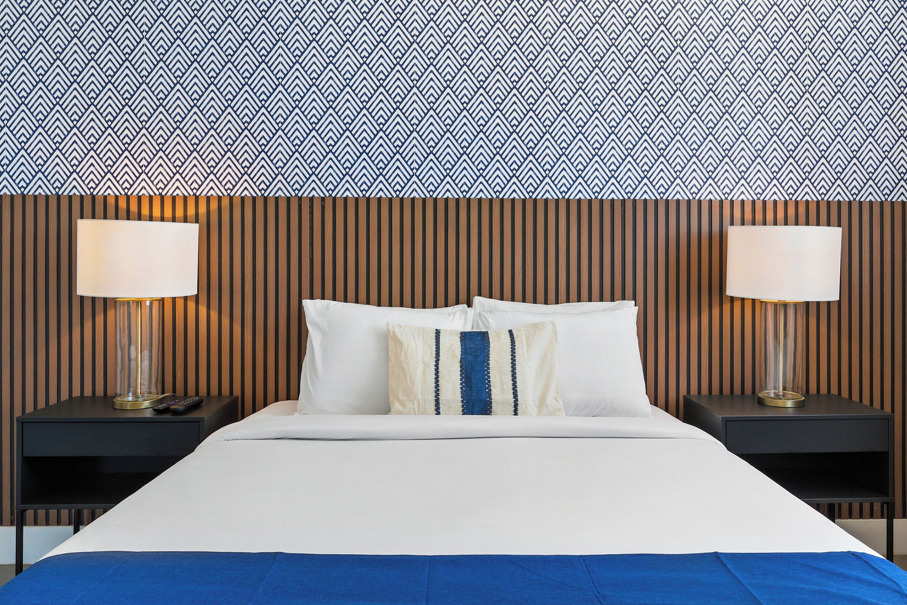 Habitación de hotel con una cama, dos mesitas de noche con lámparas y un papel tapiz estampado.