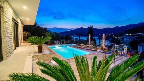 A swimming pool with lounge chairs and umbrellas, surrounded by greenery, with a view of mountains and a town in the background. - Villa Visnja - Private villa with pool, Dalmatia (Stikovica)