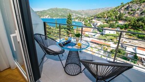 A balcony with two black wire chairs, a small round table with a glass of orange juice, and a view of a coastal town and mountains. - Villa Visnja - Private villa with pool, Dalmatia (Stikovica)